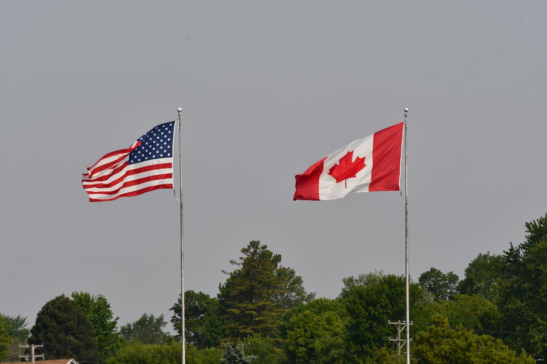 Canadian and American flags flapping in the wind on an overcast day